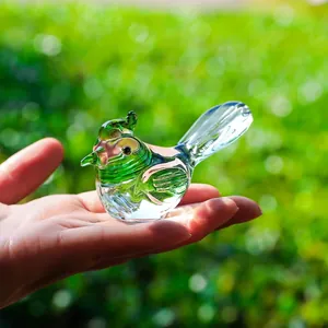 Primo piano di una statuina di uccello in cristallo verde tenuta in mano, fondo bokeh