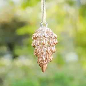 Detalle de un adorno navideño de piña de cristal con acabado dorado para jardín exterior.