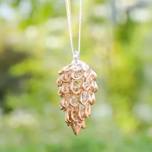Primer plano de un adorno de piña de cristal dorado colgado en un entorno de jardín.