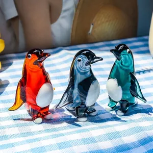 Vista dettagliata di tre figurine di pinguini in vetro colorato su tovaglia a quadri