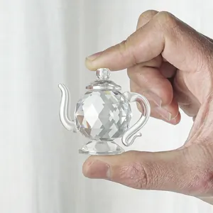 Macro detail of a faceted crystal teapot figurine held between fingers for scale