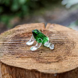 Macro detail of a faceted green and clear crystal frog figurine placed on a wooden stump.