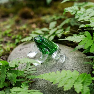 Detailed macro view of a green crystal frog figurine placed on a natural rock among ferns