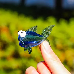 Primo piano di una mini statuetta di pesce in vetro tenuta a mano alla luce naturale