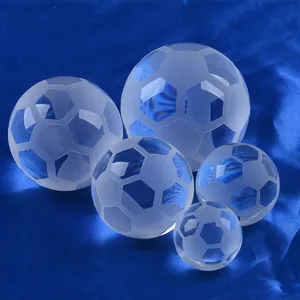 Nahaufnahme von fünf klaren Kristall-Fußball-Glasornamenten auf edlem blauem Satin.