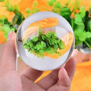 Primer plano de una mano sosteniendo una bola de cristal transparente de 70 mm con reflejos