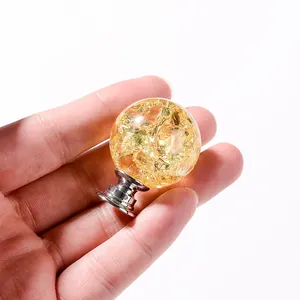 Detail view of a 3cm golden crackle crystal ball drawer knob held in hand for scale