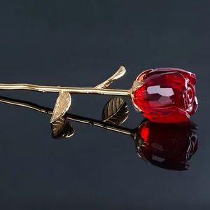 Primo piano di una rosa di cristallo sfaccettato rosso con gambo dorato su superficie nera