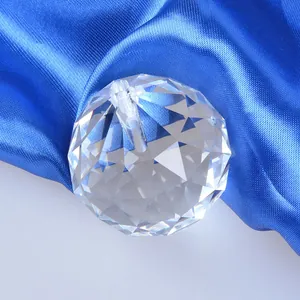 Detailed view of a multi-faceted clear crystal lighting ball pendant on blue satin fabric.