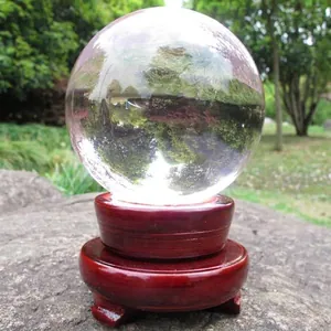 Clear 10cm crystal ball desktop ornament on wooden stand with natural outdoor reflection