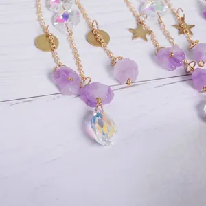 Detailed view of purple raw stones and AB color faceted crystal pendants on gold chains.