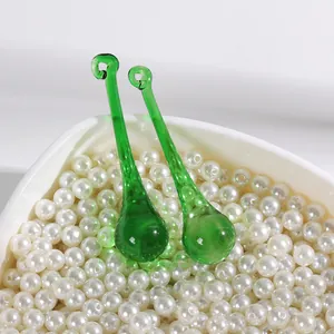 Macro detail showing two green glass waterdrop pendants nestled in a bowl of white pearls