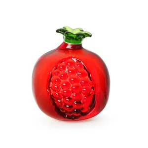 Nahaufnahme eines handgefertigten Granatapfel-Ornaments aus rotem Kristall mit grünem Stiel.