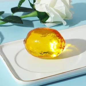 Nahaufnahme eines lichtdurchlässigen gelben Kristall-Obst-Ornaments auf einem Teller