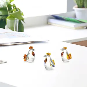 Tre figurine di gallo in cristallo colorato fatte a mano su una scrivania bianca