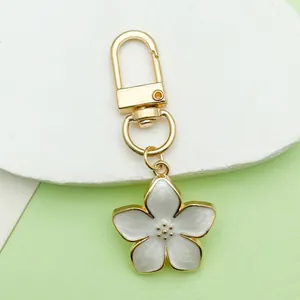 Close-up of a pearlescent white enamel flower keychain with gold-tone hardware