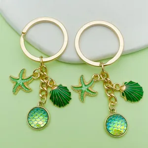 Detailed view of gold keychains featuring green enamel starfish, shell and mermaid scale charms
