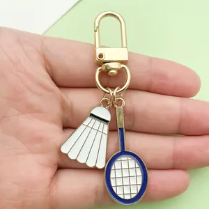 Detalle que muestra dijes de raqueta de bádminton y volante en un llavero de metal dorado.