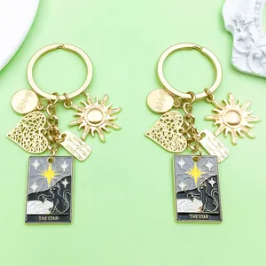 Close-up detail of two gold alloy tarot 'The Star' and black cat keychains on green surface
