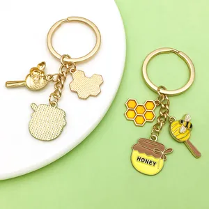 Détail des breloques émaillées en forme d'abeille et de pot de miel sur porte-clés doré