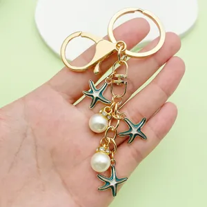 Detail showing golden starfish and pearl keychain charms on a handheld schoolbag pendant