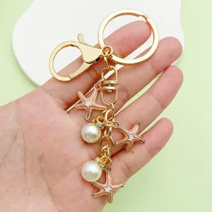 Close-up of a handmade golden keychain featuring pink enamel starfish and white pearl charms