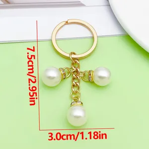 Elegante gouden sleutelhanger met drie witte parels, afmetingen 7,5 cm bij 3,0 cm.