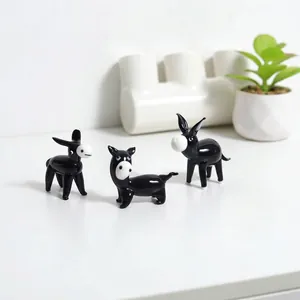 Close-up of three mini handmade black glass donkey figurines displayed on a white desk