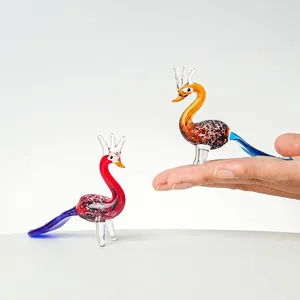 Detailansicht farbenfroher Glas-Pfauenfiguren, zur Größenbestimmung in der Hand gehalten