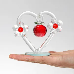 Détail de l'ornement en cristal cœur et pomme tenu en main pour montrer l'échelle.