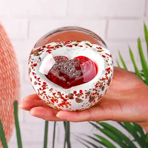 Vista dettagliata di una palla di cristallo di vetro con un cuore 3D rosso nella mano