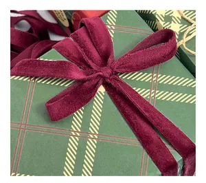 Close-up detail of a soft burgundy velvet ribbon bow tied on a green plaid festive gift box