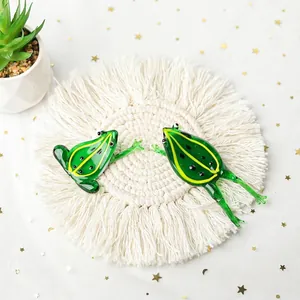 Detailed shot of two miniature green glass frog figurines on a white macramé mat