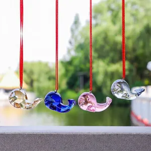 Colorful glass dolphin suncatchers hanging on red strings with blurred nature lake background