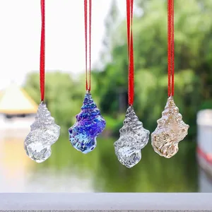 Close-up of colorful glass conch shell pendants hanging in a sunny garden setting