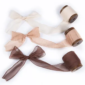 Elegant chiffon ribbons in three earth tones with rustic wooden spools on white background