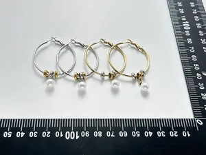 Large stainless steel hoop earrings with pearl pendants measured on a scale for size