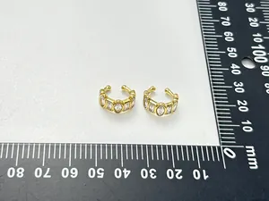 Detailed close-up view of gold-plated geometric zircon ear cuffs on a millimeter ruler