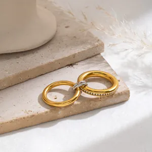 Detaillierte Nahaufnahme ineinandergreifender 18K vergoldeter Edelstahlringe mit Steinen.