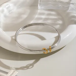 Detail eines zweilagigen Armreifs aus Edelstahl mit goldenen Ringanhängern im minimalistischen Stil.
