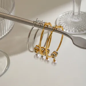 Detail view of stainless steel hoop earrings with elegant pearl pendants hanging on a rod