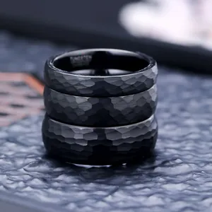 Close-up of three stacked black hammered tungsten carbide rings with matte finish