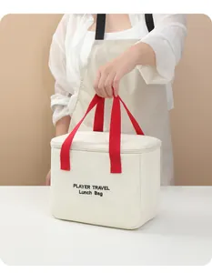 Detail view of handheld insulated cream lunch bag with red handles and embroidered text