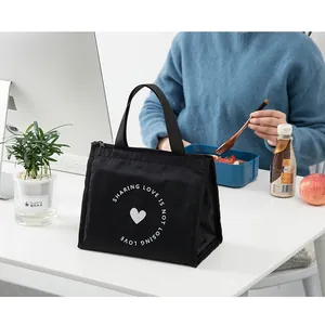 Détail du sac à déjeuner isotherme noir avec imprimé cœur sur un bureau de bureau blanc.