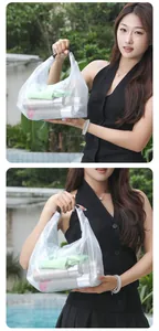 Close-up of a white mesh beach bag held by a model in an outdoor setting.