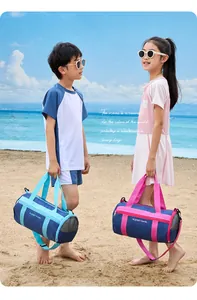 A boy and girl holding blue and pink cylindrical swim bags on a sandy beach