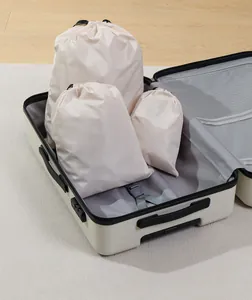 Close-up of three beige drawstring travel organizer bags inside a white suitcase