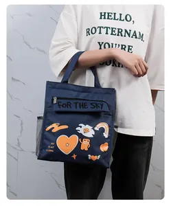 Detail shot of a navy blue insulated lunch bag with cute cartoon patches held by a model.