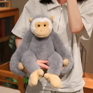 Soft and cuddly long-armed grey gibbon plush toy held in a warm lifestyle indoor setting.