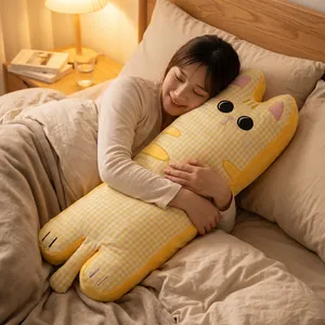 Modèle tenant un oreiller long en forme de chat jaune à carreaux sur un lit confortable.